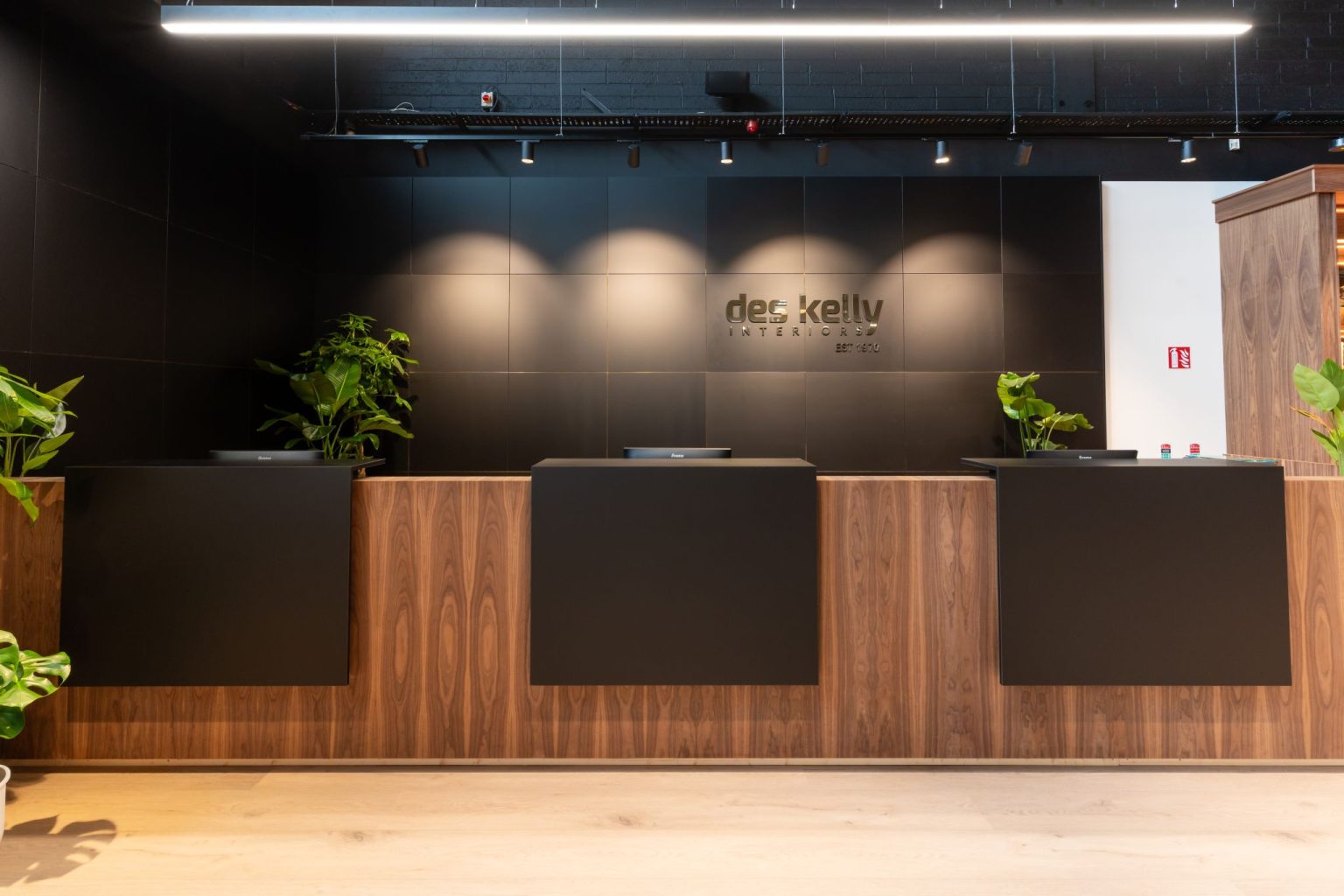 Walnut and matt black reception counter in front of a black panelled wall carrying the Des Kelly Interiors sign