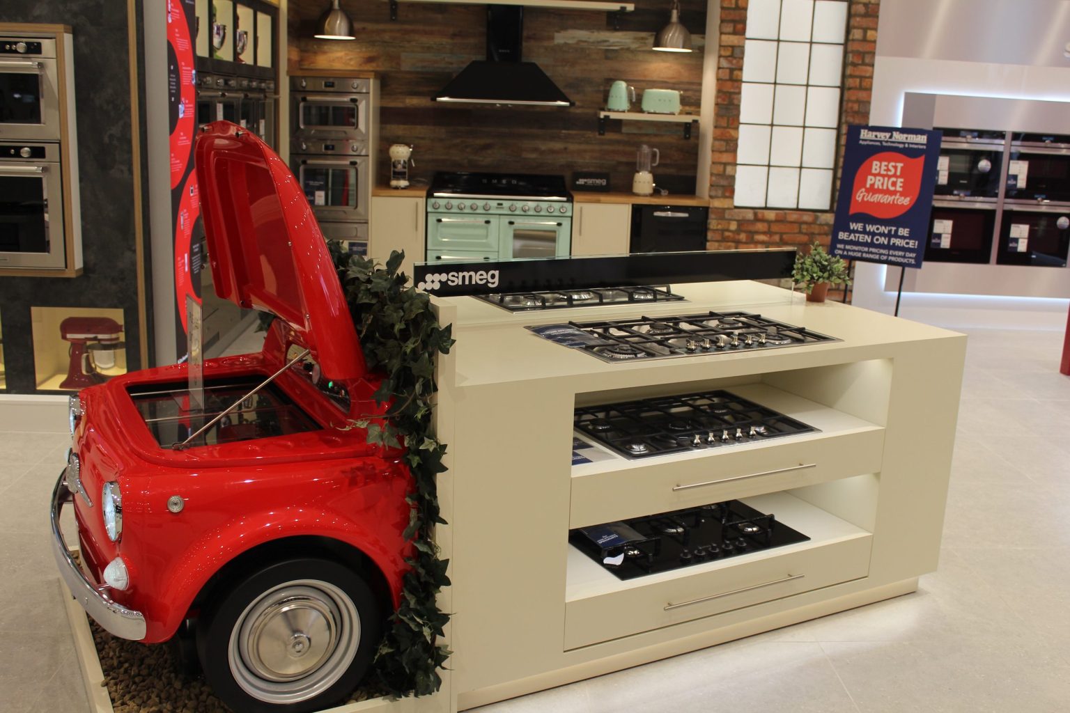 Smeg display with a cream island of built-in gas hobs beside the front of a red Fiat 500, in an electrical retail showroom