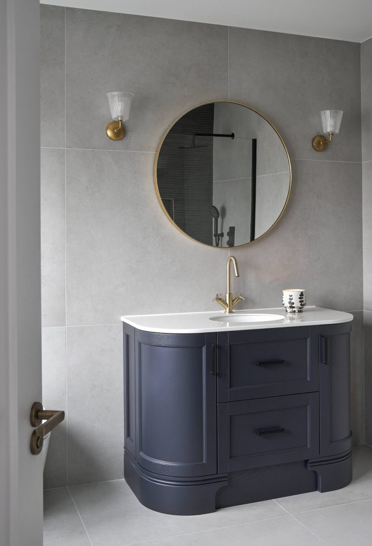 Mount Alton bathroom vanity with round mirror, gold fixtures, and blue cabinet.