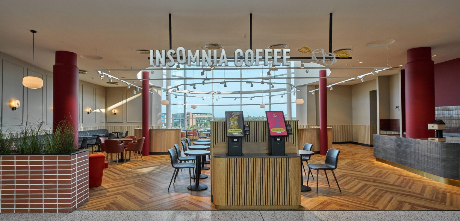 Insomnia Coffee at Liffey Valley Shopping Centre with a timber-slatted order kiosk, red columns, café tables and a herringbone floor