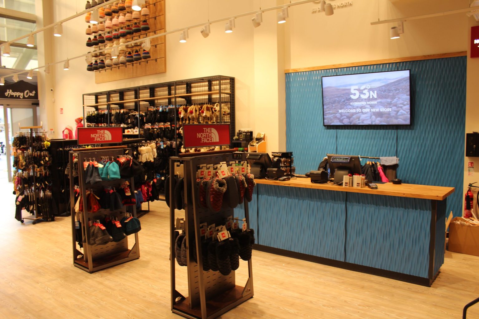 Service counter with a blue textured panelled front and a timber top beside black metal stands of gloves and hats in the 53 Degrees North store