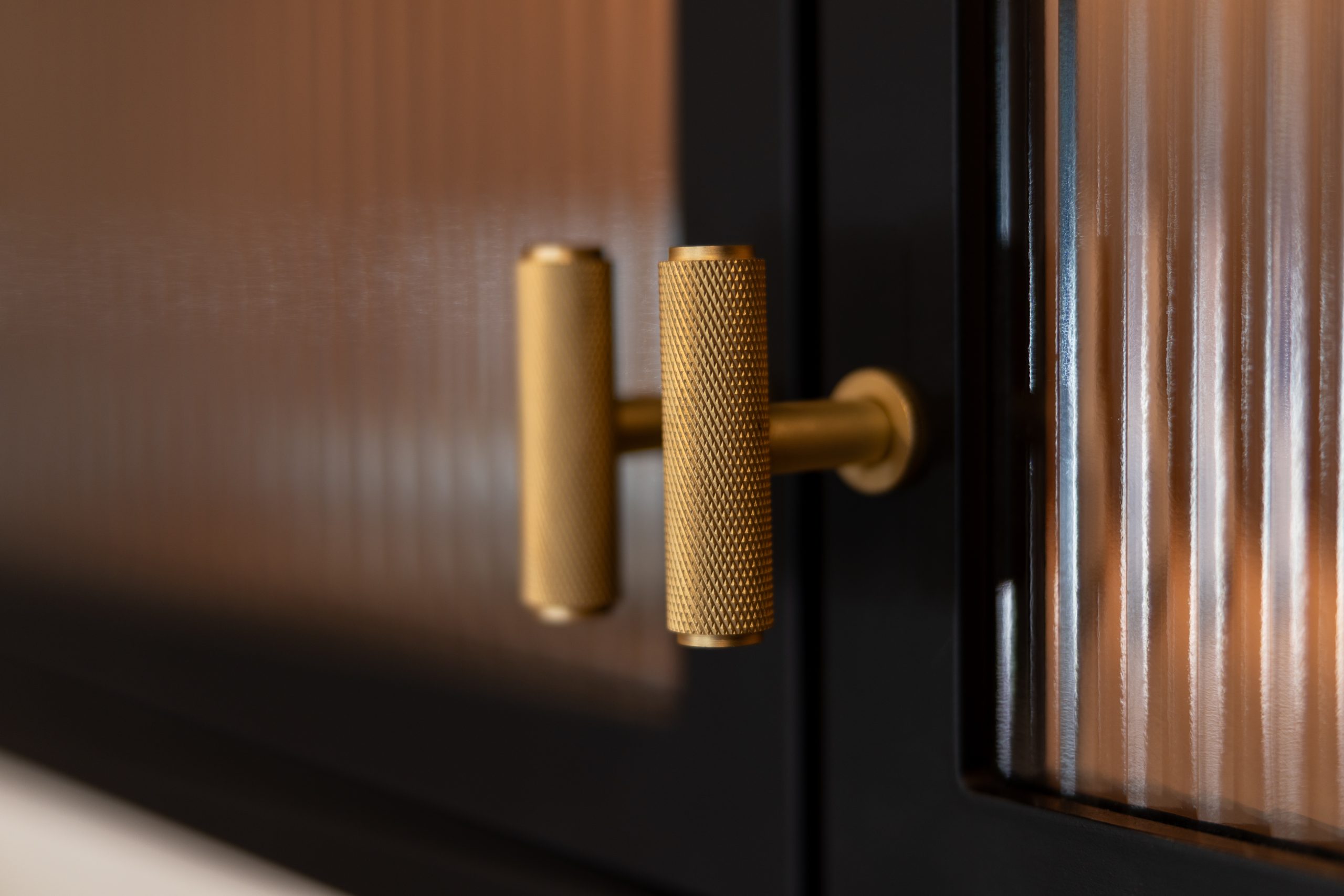 Close-up of a knurled brass T-bar handle on a dark walnut and black bespoke kitchen cabinet door