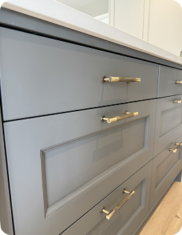 Close-up of modern gray drawers with gold handles beneath a white countertop, showcasing a sleek and contemporary cabinet design.