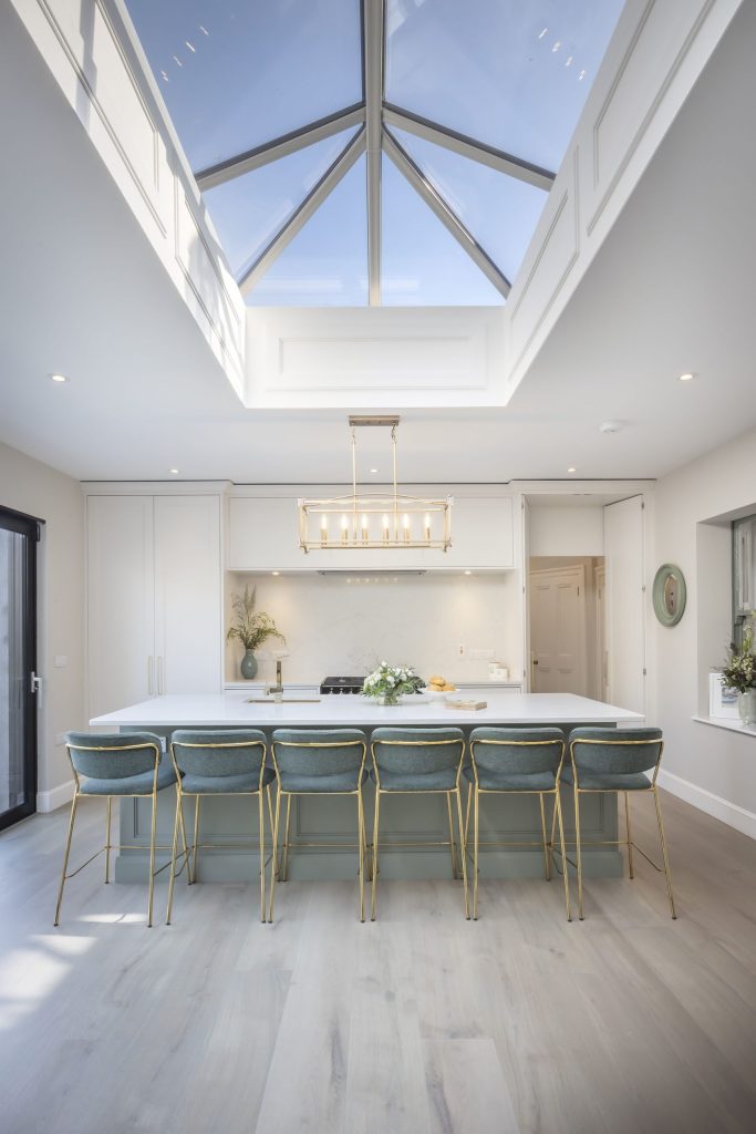Large kitchen island, stone worktop gold & green chairs. Large Skylight
