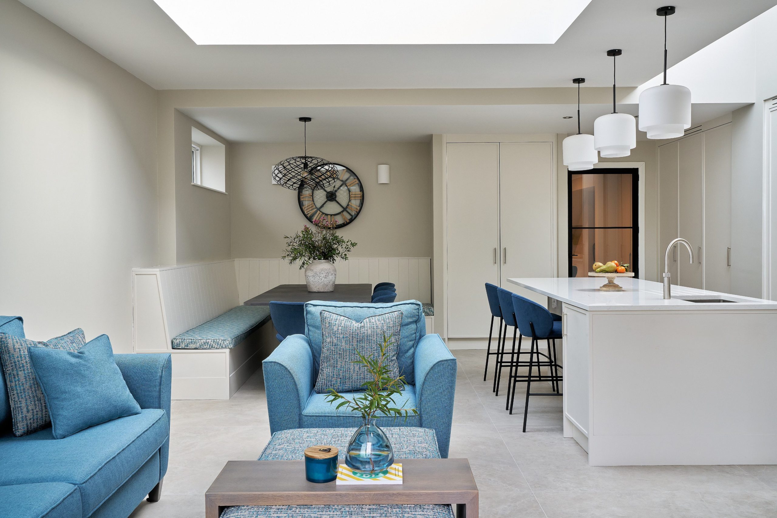 Open-plan living and kitchen space with a blue sofa, white island, pendant lights and a rooflight
