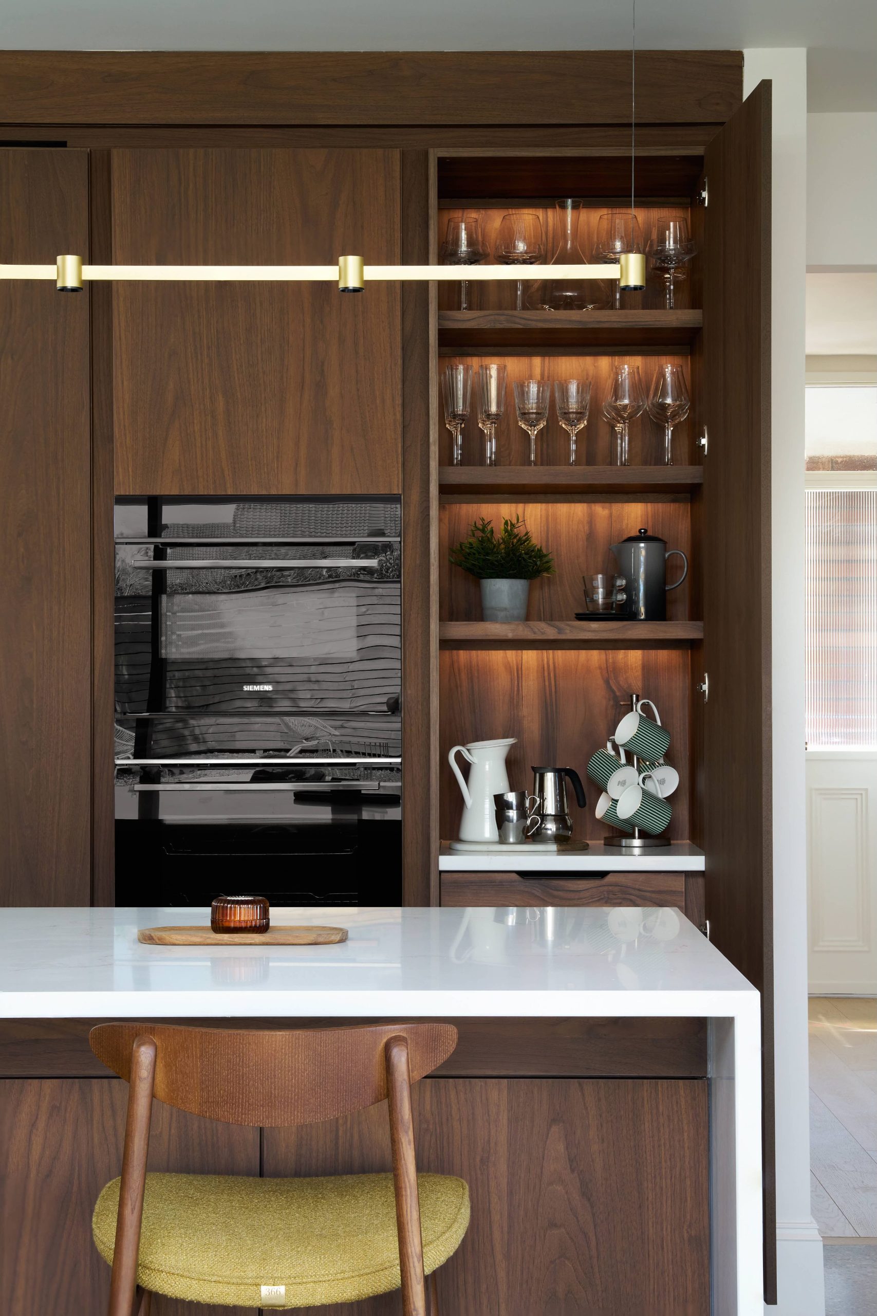 Dark walnut kitchen tower with a Siemens oven, LED-lit open shelving and a gold pendant