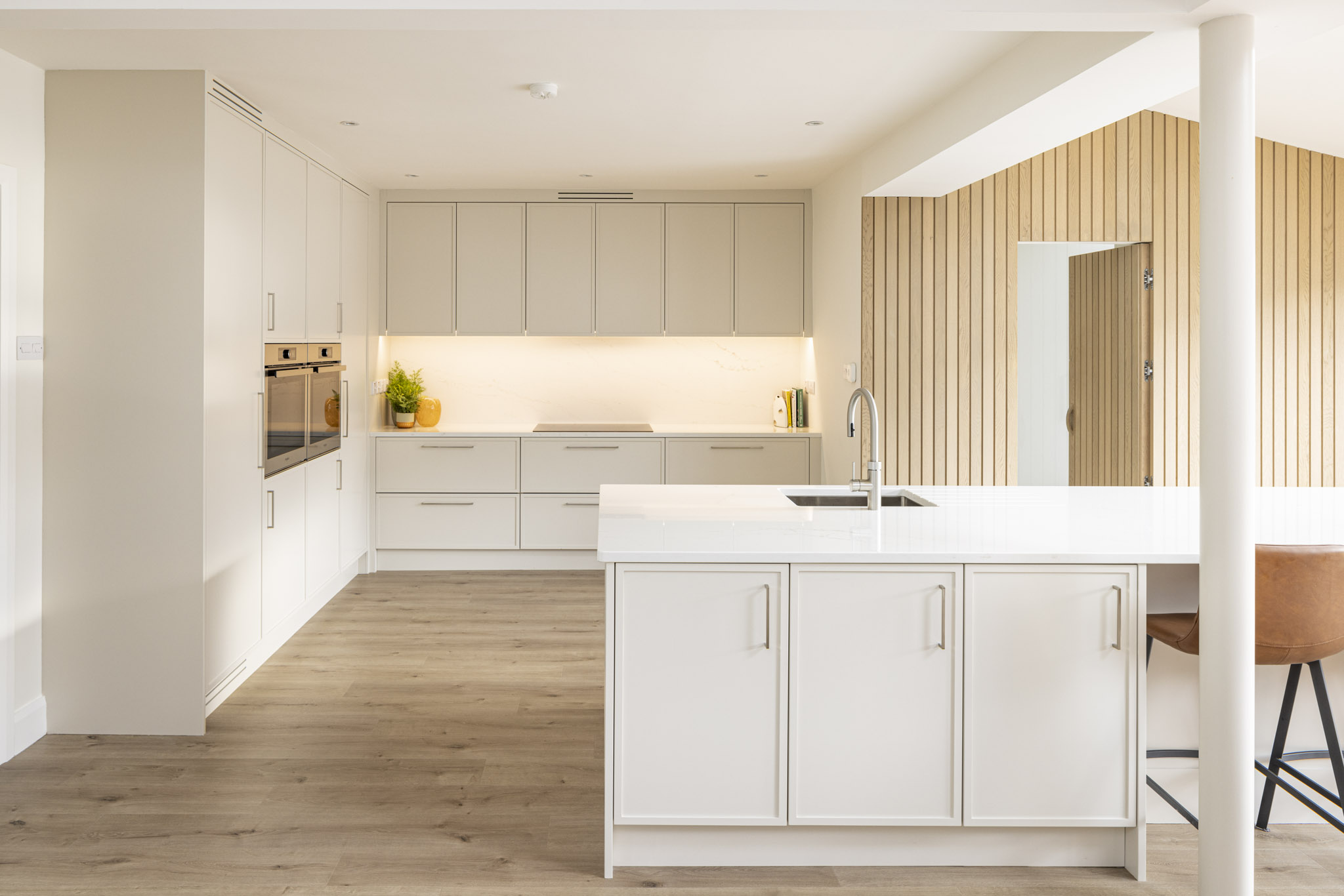 Large open-plan white kitchen extension in a Dublin home with wood wall panelling, island and concealed door by ONOVO