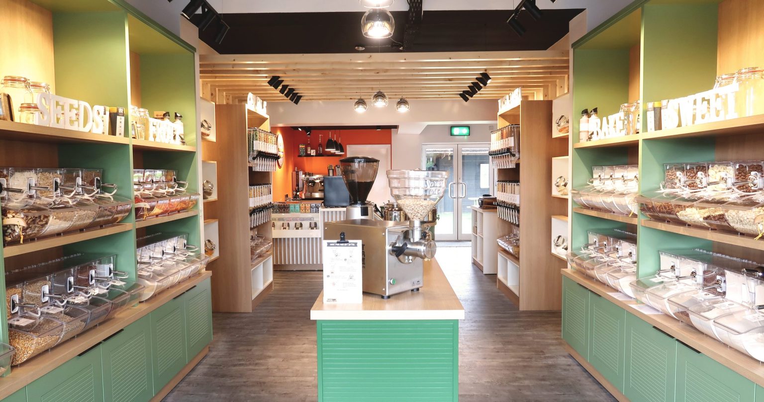 Proper Shopper zero-waste store in Leopardstown with timber shelving of bulk dispensers above green base cabinets and a central island